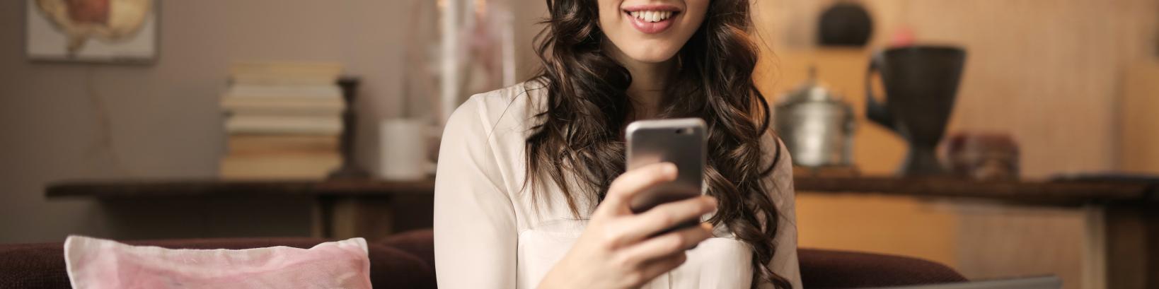 a women holding a mobile phone in front of a laptop