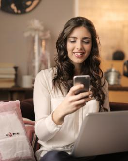 a women holding a mobile phone in front of a laptop