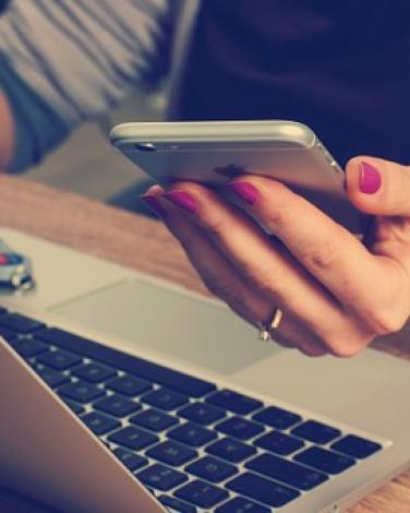 a mobile phone in a woman's hand over an open laptop